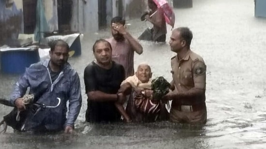 Locals help an elderly woman move through a waterlogged street as heavy rain disrupts normal life, in Rajkot.(ANI)