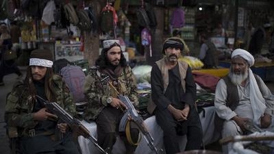 Taliban fighters sit next to street vendors at a local market in Kabul on September 10. (File photo)