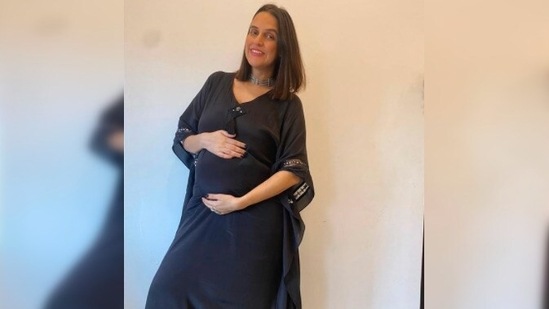 Neha Dhupia holds her baby bump as she poses in a simple yet elegant black kaftan.(Instagram/@gumanistylists)
