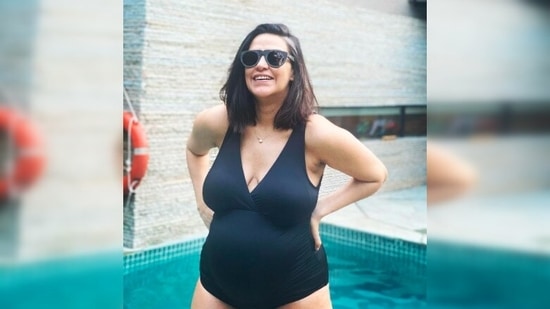 Pregnant Neha Dhupia poses near the pool in a black swimsuit.(Instagram/@nehadhupia)