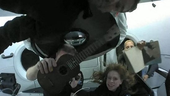 This screengrab taken from the SpaceX live webcast shows Inspiration4 crew members (from L) Jared Isaacman, Christopher Sembroski holding up a ukelele, Hayley Arceneaux and Sian Proctor holding up her artwork while in orbit. - The first space tourism mission by Elon Musk's SpaceX blasted off from Florida on September 15 and the four crew members -- a billionaire and three other Americans -- have already seen more than 25 sunsets and sunrises. (Handout / SPACEX / AFP) This screengrab taken from the SpaceX live webcast shows Inspiration4 crew members (from L) Jared Isaacman, Christopher Sembroski holding up a ukelele, Hayley Arceneaux and Sian Proctor holding up her artwork while in orbit. - The first space tourism mission by Elon Musk's SpaceX blasted off from Florida on September 15 and the four crew members -- a billionaire and three other Americans -- have already seen more than 25 sunsets and sunrises. (Handout / SPACEX / AFP)