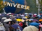 People wearing raincoats and carrying umbrellas walk through a plaza near the entrance of Universal Studios Beijing in Beijing, Monday, Sept. 20, 2021. Thousands of people brave the rain visit to the newest location of the global brand of theme parks which officially opens on Monday.