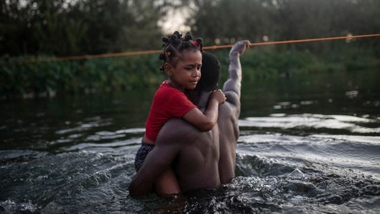 A Haitian migrant carries a child while wading across the Rio Grande from Del Rio, Texas, to return to Ciudad Acu?a, Mexico, on Sept. 19. Of the roughly 1.8 million Haitians living outside their homeland, the United States is home to the largest Haitian immigrant population in the world, numbering 705,000 people from the Western Hemisphere's poorest country, AP reported.(Felix Marquez / AP)