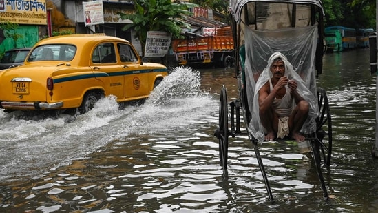 A rickshaw-puller wraps himself with plastic sheet while waiting to ferry customers across a waterlogged streets of Kolkata.(AFP)