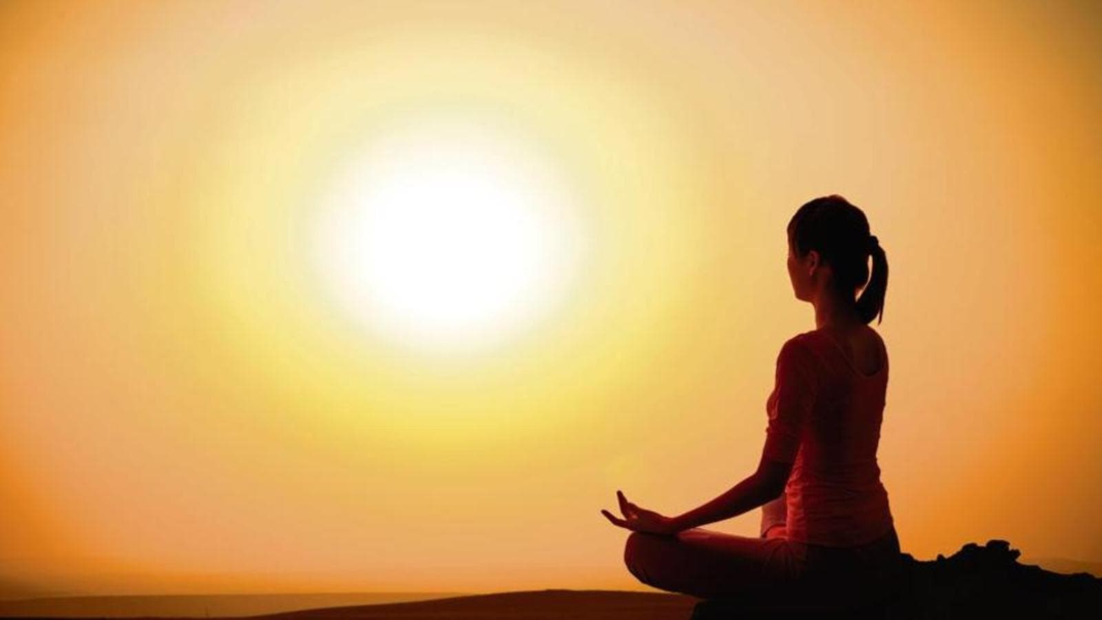  The image is of a woman meditating in a yoga pose with a sun rising over the horizon.