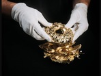 The image shows the sculpture of avocado bagel made using gold.