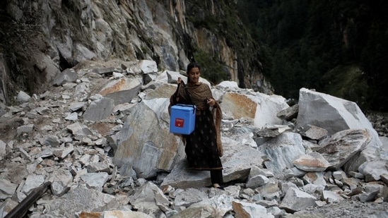 Kanta Devi, 26, a health worker, carries a box containing Covishield vaccines, as she walks through a road that was blocked after a landslide, near Malana village in Himachal Pradesh, on September 14. To vaccinate the villagers of Malana, one challenge to overcome by health workers was the steep topography, moreover to walk on it for hours and another was religious beliefs, as the tourism-dependent state immunised its roughly 5 million adults, Reuters reported.(Adnan Abidi / REUTERS)