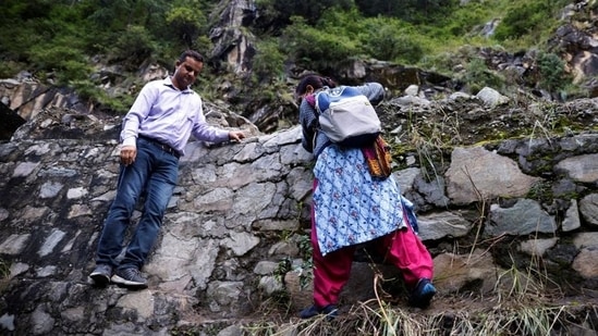 Bimla Thakur, 56, a health worker, treks through mountains to vaccinate people, near Malana village in Himachal Pradesh, on September 14. Blocked by the landslide, they left their vehicle with two blue vaccine boxes slung over their shoulders to manoeuvre over the rubble, climb the wall and then walk to the trailhead leading to the village, accompanied by a Reuters photographer. (Adnan Abidi / REUTERS)