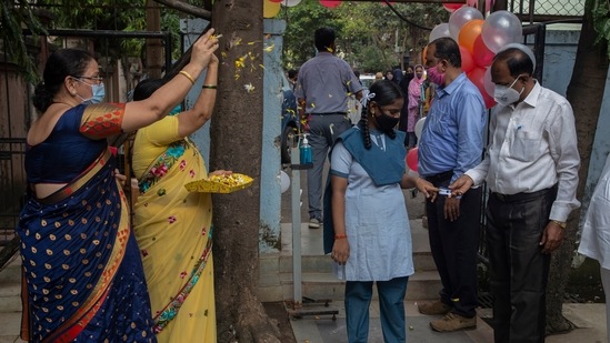 Staff members of a school in Mumbai shower flower petals and check temperature while welcoming students during the partial reopening in Dharavi.(AP Photo) Staff members of a school in Mumbai shower flower petals and check temperature while welcoming students during the partial reopening in Dharavi.(AP Photo)