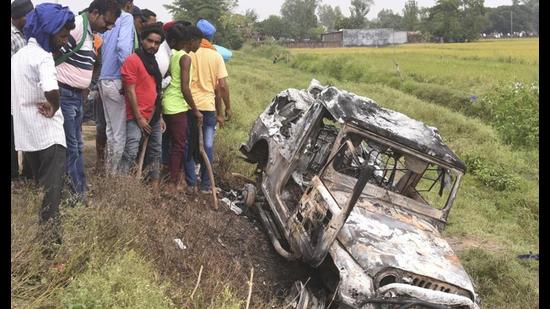 Villagers watch a burnt car which allegedly ran over and killed farmers on Sunday, at Tikonia village in Lakhimpur Kheri. (AP Photo)