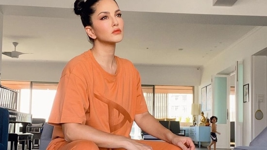 Completing her attire with a pair of white socks and a pair of beige sneakers, Sunny posed on the couch as the cameras caught her son cutely roaming bare-chested in the backdrop. (Instagram/sunnyleone)