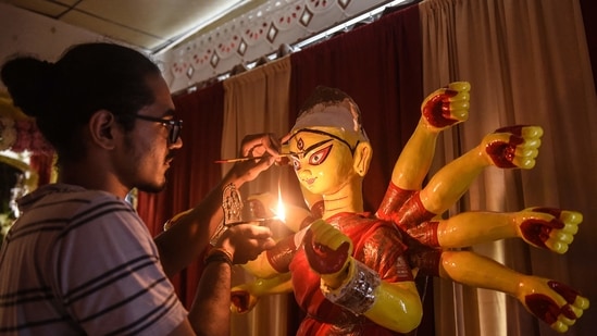 An artist in Ahmedabad holds a diya in his right hand and paints Goddess Durga's eyes with his left hand ahead of the main celebrations of Durga Puja.(AFP)