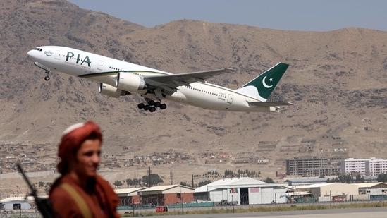 A Taliban fighter stands guard as a Pakistan International Airlines plane takes off with passengers onboard at the airport in Kabul.(AFP)