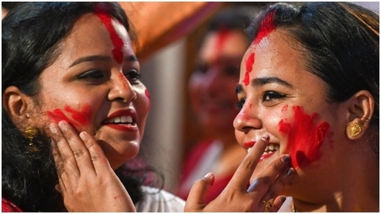 Two women are seen indulging in sindoor khela as they smile with all their hearts.(AFP)