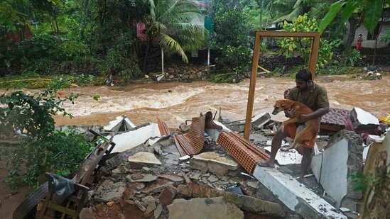 A man carries a dog amid the debris of his damaged house after flash floods caused by heavy rain at Thodupuzha in Kerala.&nbsp;(AFP File Photo)