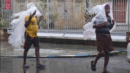 People cover themselves with plastic sheets walk on a road during rain in Kolkata. (PTI Photo)