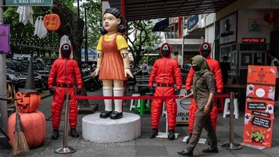 A woman walks past statues featuring characters from the Netflix series Squid Game at a food court to attract visitors in Surabaya. (AFP) A woman walks past statues featuring characters from the Netflix series Squid Game at a food court to attract visitors in Surabaya. (AFP)