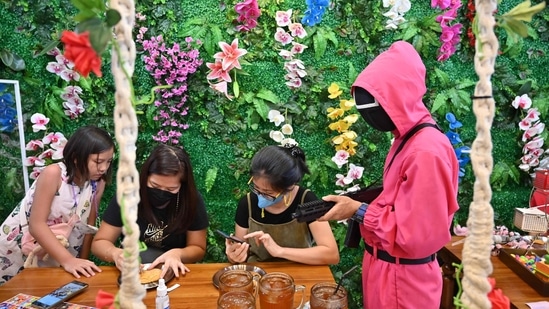 Women make dalgonas as a waiter dressed in an outfit from the Netflix series Squid Game watches them.(AFP)