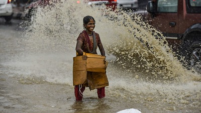 A woman drenched in rainwater reacts while crossing a road after heavy rains in New Delhi. IMD said southwest monsoon withdraws from country. (PTI)