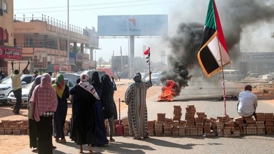 Sudanese protesters lift national flags next to a brick roadblock during a demonstration in the capital Khartoum, on October 25, 2021, to denounce overnight detentions by the army of members of Sudan's government. (AFP Photo) (AFP) Sudanese protesters lift national flags next to a brick roadblock during a demonstration in the capital Khartoum, on October 25, 2021, to denounce overnight detentions by the army of members of Sudan's government. (AFP Photo) (AFP)