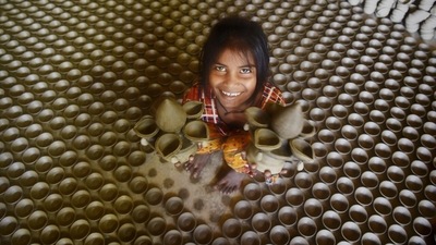 A young member of the family holds two big diyas in both her hands and smiles for the camera. (HT Photo/Deepak Gupta)