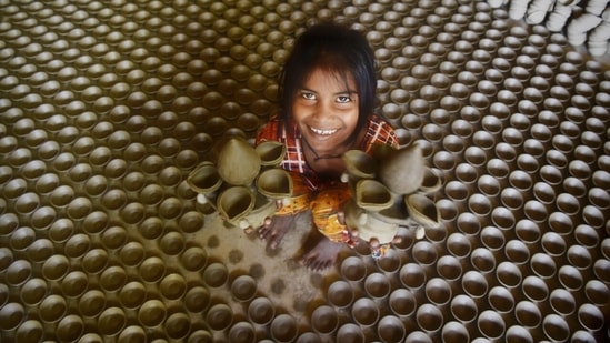 A young member of the family holds two big diyas in both her hands and smiles for the camera.(HT Photo/Deepak Gupta)