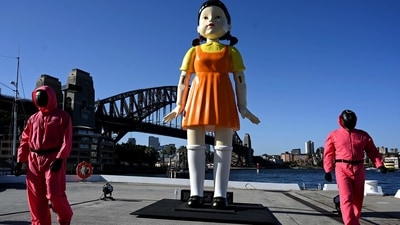 Cosplayers stand next to a 4.5 metre tall replica doll from the Netflix series Squid Game on display at the harbour in Sydney. (AFP) Cosplayers stand next to a 4.5 metre tall replica doll from the Netflix series Squid Game on display at the harbour in Sydney. (AFP)