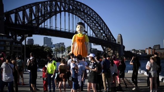 People on social media are sharing Squid Game related content and receiving good response from their fans. In Sydney, a 4.5 metre tall replica doll from the Squid Game has installed at the harbour and fans and rushing to take pictures with the doll.(AFP)