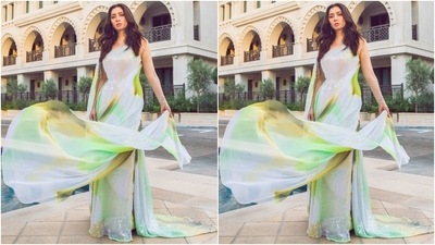 Mahira's gown, decorated with patterned sequins in green, brown, and yellow hues, features a one-shoulder neckline with the other sleeve extending into a flowy train, embellishments on the waist, a bodycon fit, and a floor-sweeping train. 