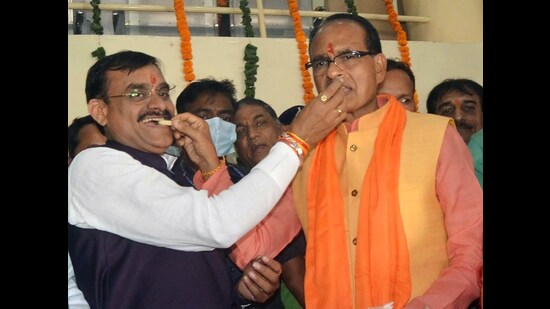 Madhya Pradesh Chief Minister Shivraj Singh Chouhan and Bharatiya Janata Party (BJP) State President VD Sharma offer sweets to each other as the party leads in State assembly by-elections, at BJP State Headquarters, in Bhopal on Tuesday. (ANI)