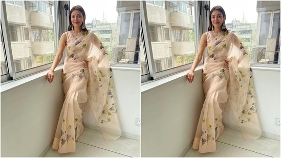The off-white organza saree Kajal chose for Diwali festivities comes adorned with greyish and green floral patterns and gold sequinned embroidery all over the drape. She teamed the six yards with an off-white sleeveless blouse featuring a U neckline.(Instagram/@sayali_vidya)