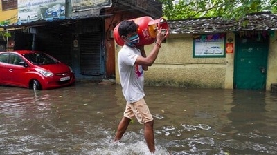 A man carries a cooking gas cylinder and wades past a waterlogged street in Chennai as the city witnesses torrential showers for the second time in five days. (AP)