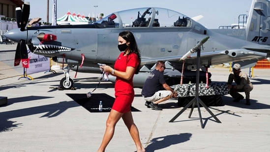 A woman walks past a Beechcraft AT-6 Wolverine light-attack aircraft as crew members install a device to its wing at the Dubai Air Show.(AP)