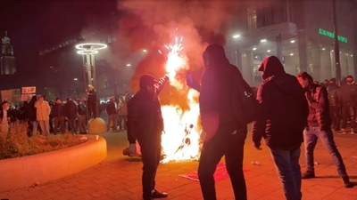 A man stands with a flare as protesters watch a motorcycle burning in Rotterdam, Netherlands November 20, 2021, in this screen grab obtained from a social media video. (via REUTERS)