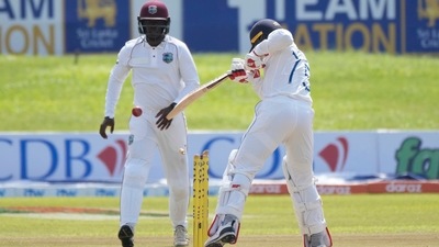 Sri Lankan batter Dhananjaya de Silva hits the wicket while attempting to stop the ball being fallen on it as West Indies' fielder Nkrumah Bonner watches during the day two of first Test match. (AP)