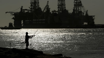 FILE - A man wears a face mark as he fishes near docked oil drilling platforms, Friday, May 8, 2020, in Port Aransas, Texas. (AP) FILE - A man wears a face mark as he fishes near docked oil drilling platforms, Friday, May 8, 2020, in Port Aransas, Texas. (AP)