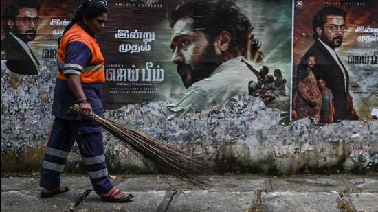 A sanitation worker walks past a poster of actor Suriya from the film Jai Bhim in Chennai. (AFP/File)