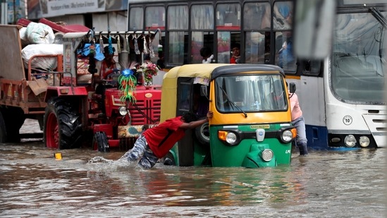 An auto rickshaw driver pushes his vehicle through a flooded street after heavy rains affected normal life in Bengaluru.(AP)