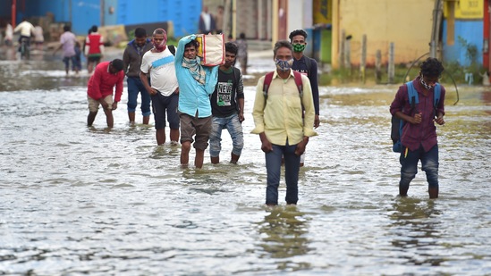 People wade through a waterlogged road which was caused due to overnight rain and breach of adjacent lake wall in Bengaluru.(PTI)
