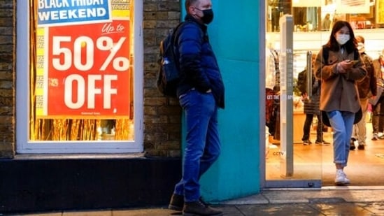 A person wears a mask as he stands close to a Black Friday sign in Covent Garden, in London.(AP)