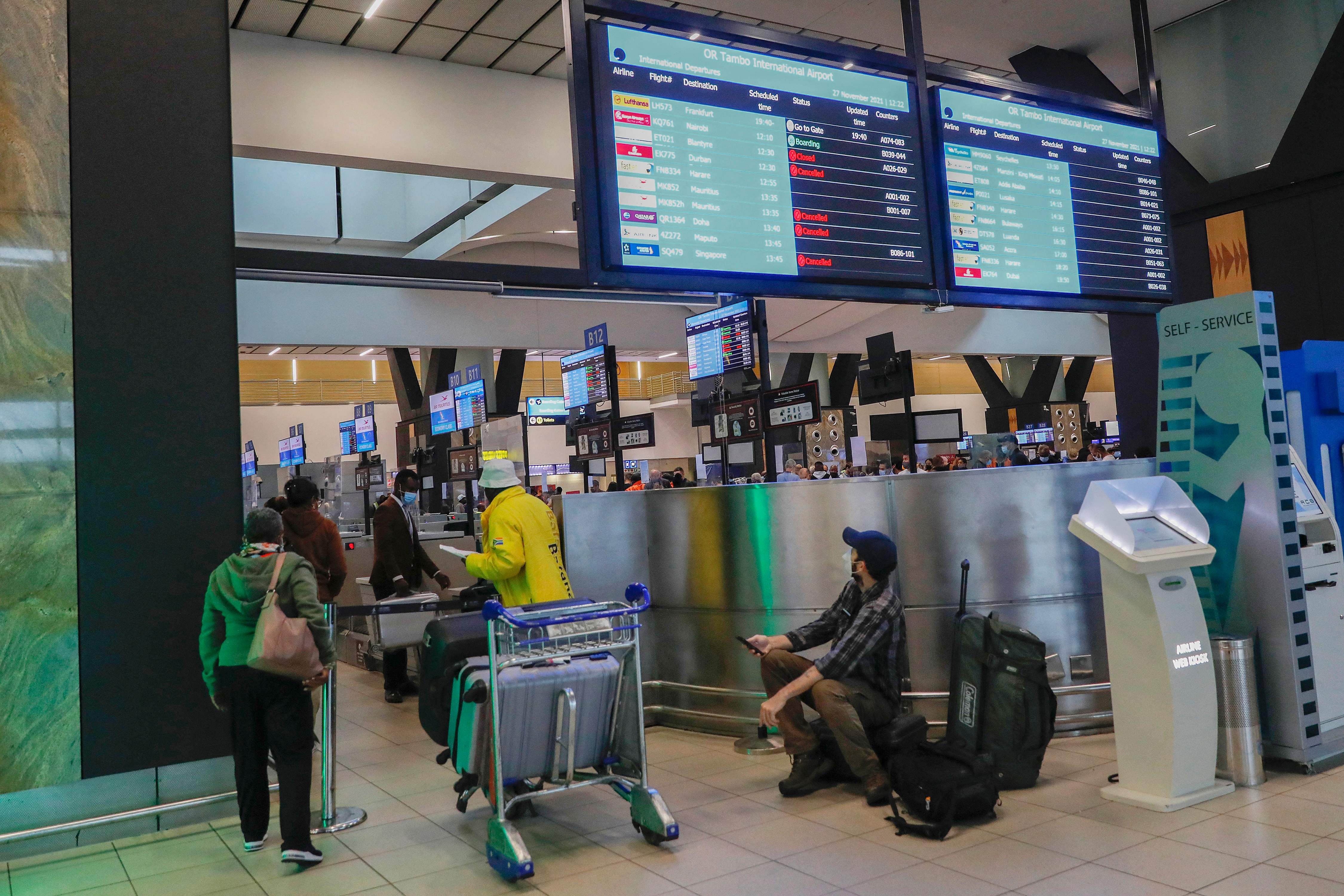 A passenger holds his mobile phone while looking at an electronic flight notice board displaying cancelled flights at OR Tambo International Airport in Johannesburg, on November 27, 2021, after several countries banned flights from South Africa following the discovery of a new Covid-19 variant Omicron. (Photo by Phill Magakoe / AFP)
