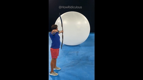 The image shows the man aiming at the huge balloons.(Instagram/@howridiculous)