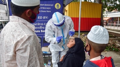 A medic collects sample from a passenger for COVID-19 test, at KSRTC bus stand in Bengaluru on Sunday. (PTI Photo) A medic collects sample from a passenger for COVID-19 test, at KSRTC bus stand in Bengaluru on Sunday. (PTI Photo)