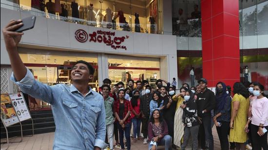 A group of young people, many wearing face masks as a precaution against Covid-19, pose for a selfie outside a shopping mall in Bengaluru, capital of Karnataka. India on Thursday confirmed its first two cases of the omicron coronavirus variant in two men in Karnataka including one who came from abroad.. (AP)