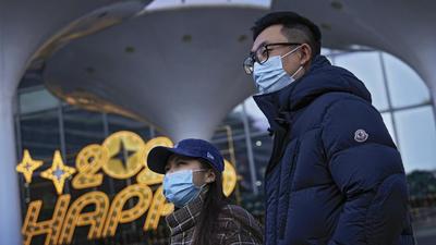 People wearing face masks to help curb the spread of the coronavirus walk by a shopping mall displaying an illuminated welcome year 2022, in Beijing. (AP) People wearing face masks to help curb the spread of the coronavirus walk by a shopping mall displaying an illuminated welcome year 2022, in Beijing. (AP)