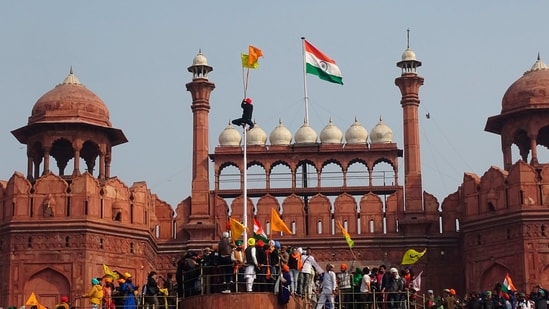 A man hangs on to a pole holding a Sikh religious flag along with a farm union flag at the historic Red Fort during the farmers protest against new farm laws.&nbsp;(AP File Photo)
