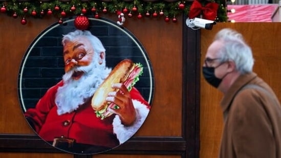 A man wears a face mask as he walks past an image of Santa Claus at a Christmas market, in London(AP)