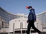 A man wearing a mask walks past the headquarters of the People's Bank of China, the central bank, in Beijing, China.