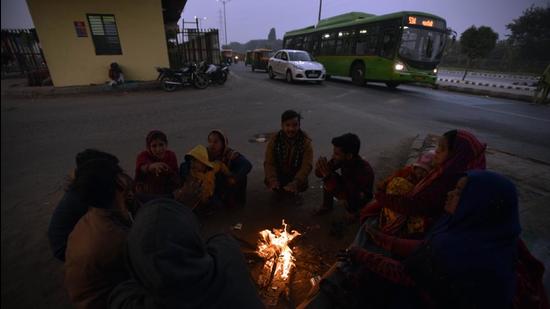 People huddle around a bonfire at Sarai Kalen Khan, on Wednesday evening. (Sanjeev Verma/HT PHOTO)
