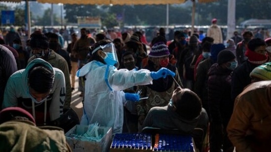 A health worker collects a swab sample of a passenger to test for Covid-19 as others wait for their turn at a train station in New Delhi.(AP) A health worker collects a swab sample of a passenger to test for Covid-19 as others wait for their turn at a train station in New Delhi.(AP)